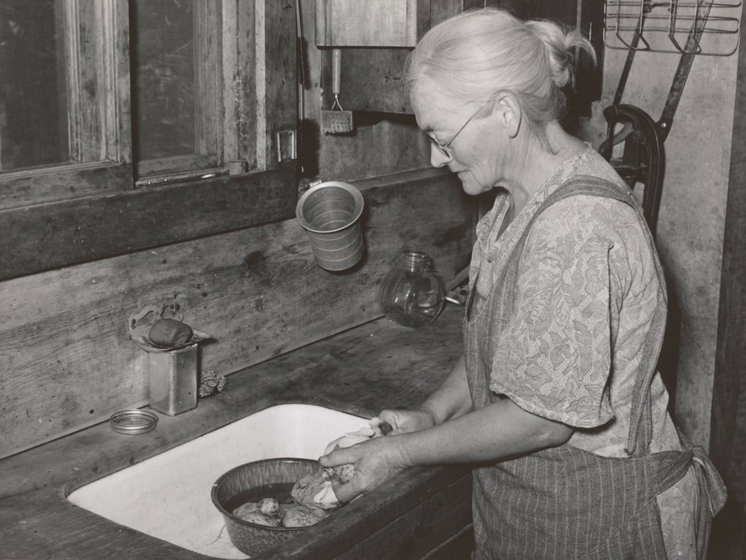 grayscale photography of woman standing beside sink