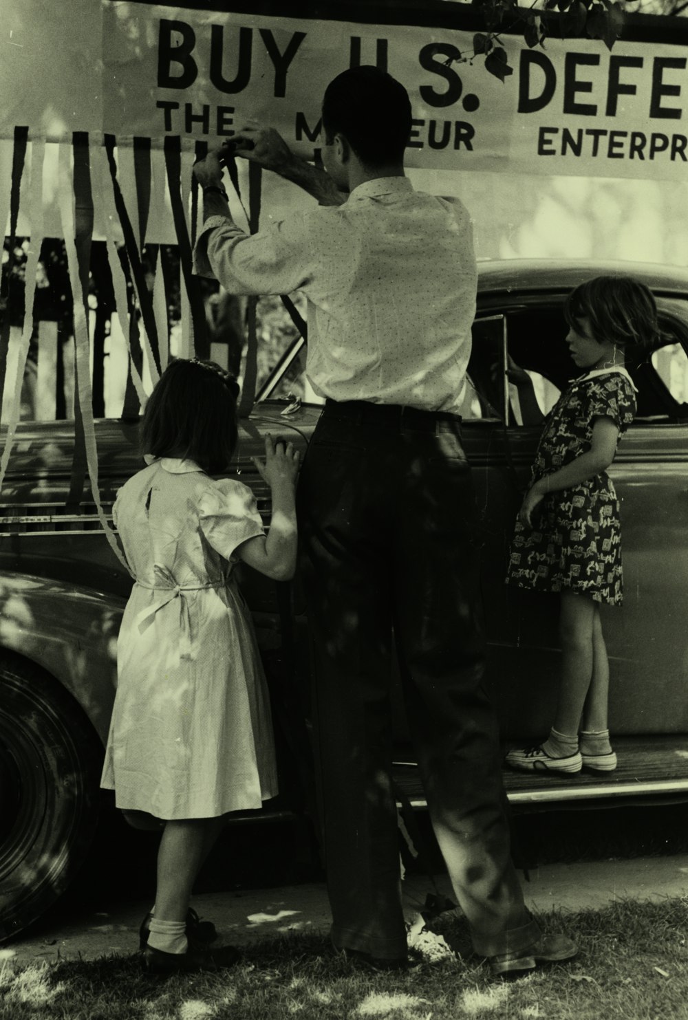 fotografia em tons de cinza de homem e duas meninas ao lado do veículo