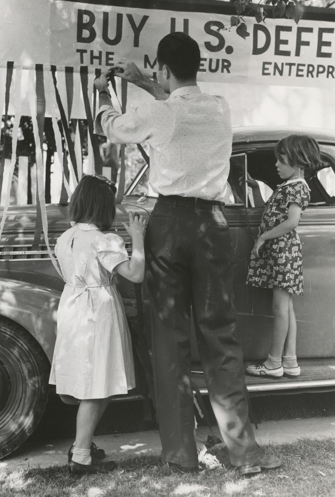 grayscale photography of man and two toddler girls beside vehicle