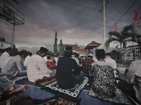 Community members praying together outdoors under a clear blue sky.