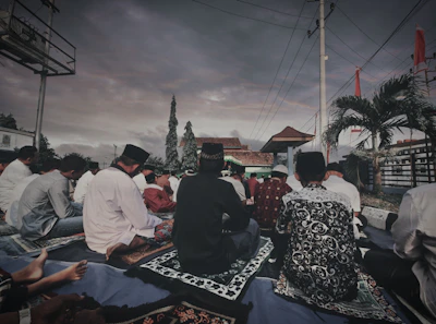 Community members praying together outdoors under a clear blue sky.