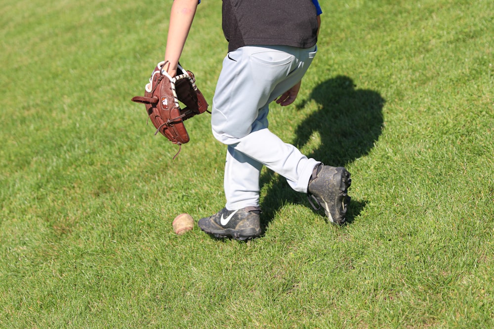 man standing on grass field picking up baseball