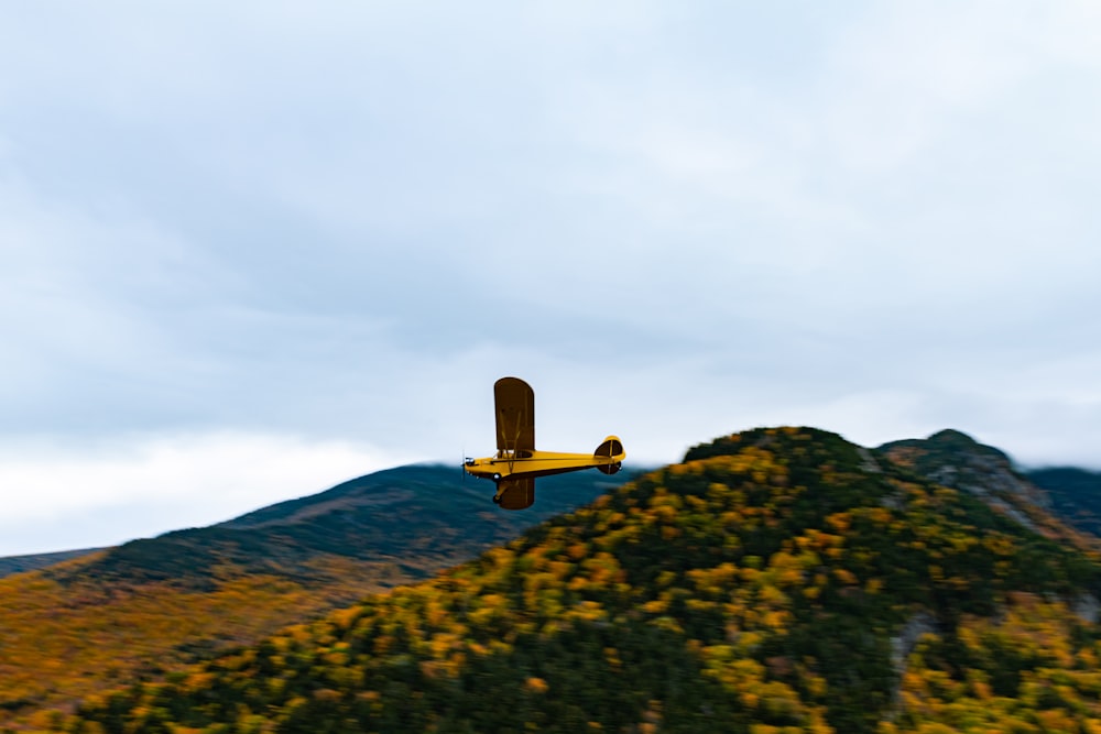 yellow biplane flying over hill
