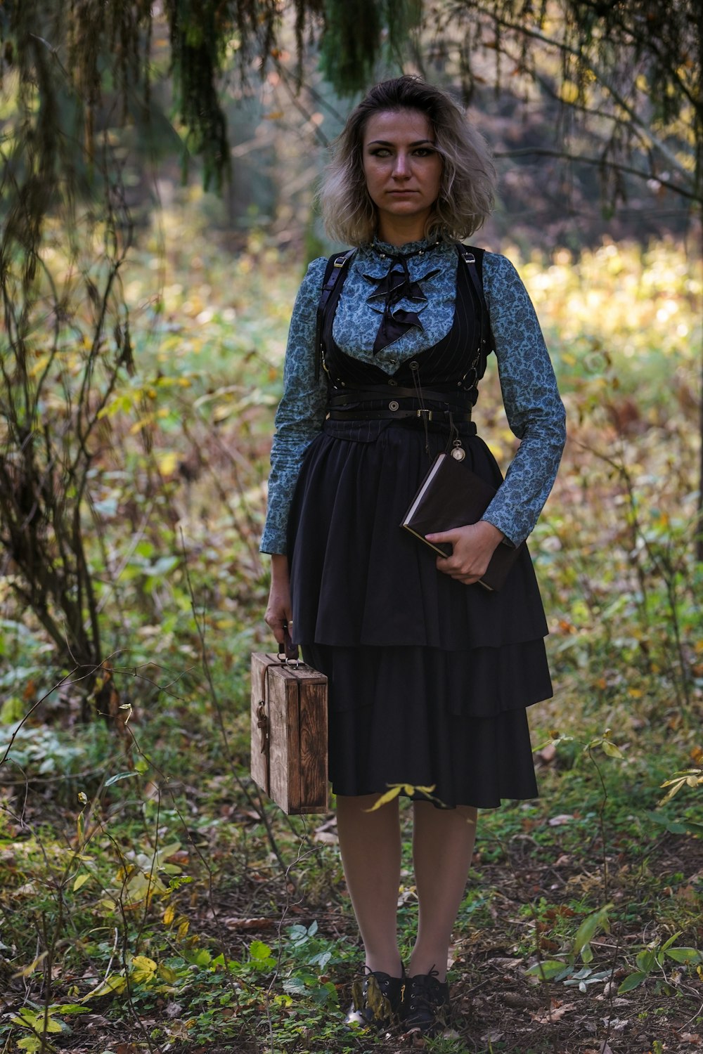 woman standing on grass while holding book and suitcase