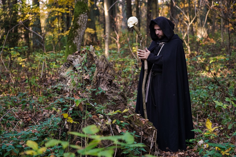 man wearing cloak and holding a wooden cane with white skull ornament