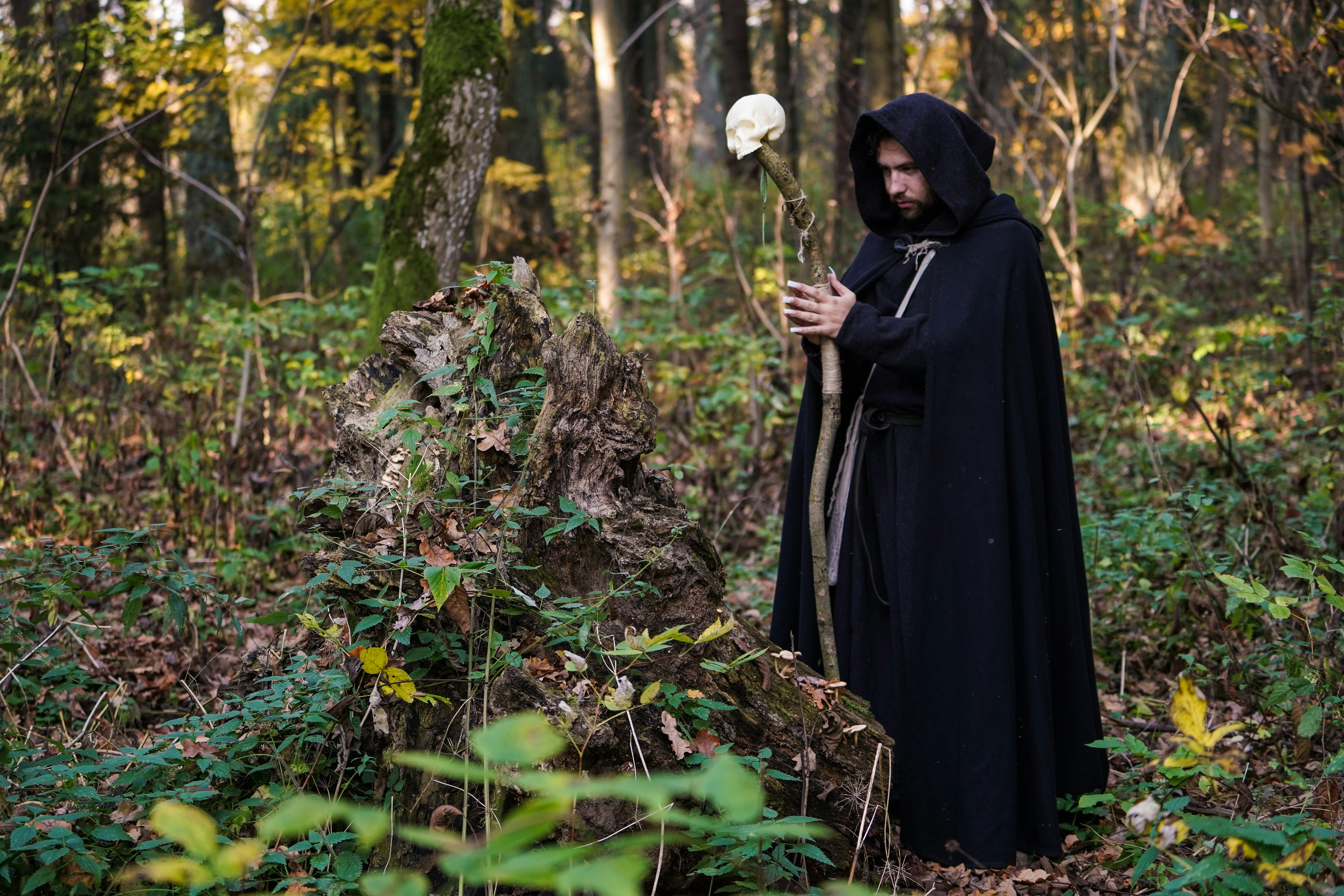 man wearing cloak and holding a wooden cane with white skull ornament