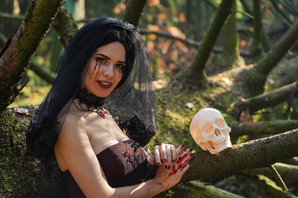 mujer con disfraz de Halloween sentada en un árbol junto a un cráneo humano blanco