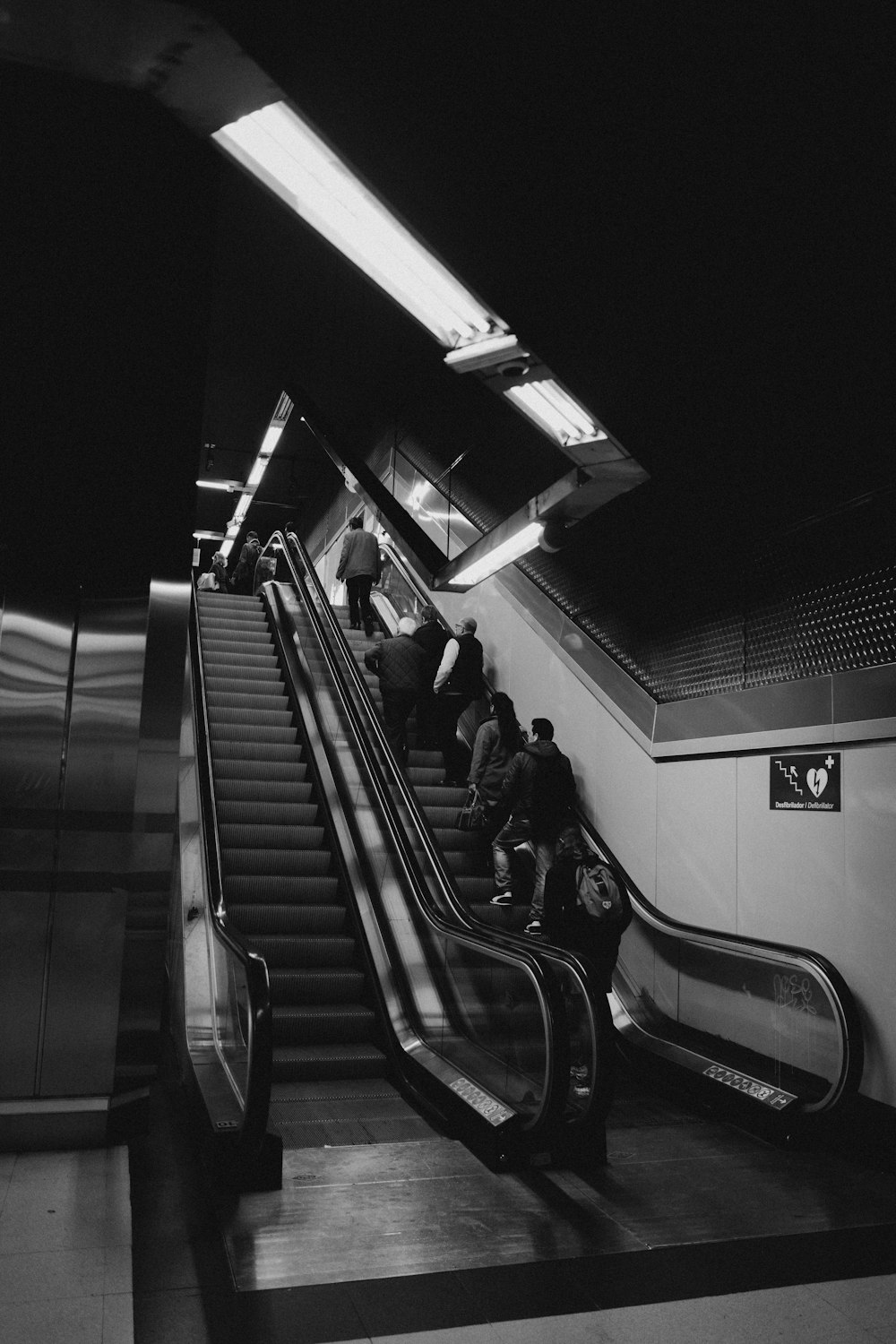 greyscale photo of people standing on subway escalator