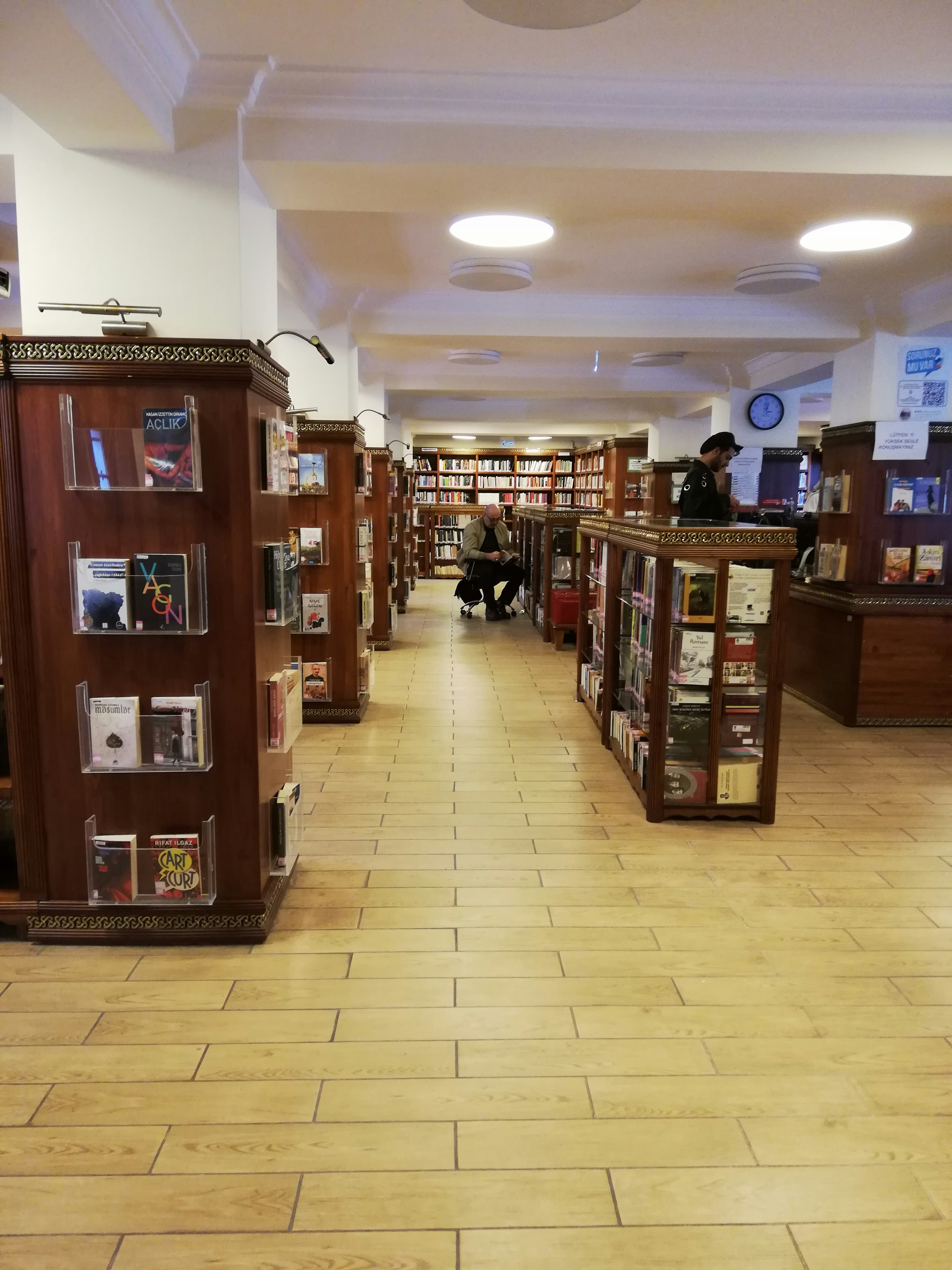 Young students reading books and writing in notebooks in a well-lit library with wooden shelves in the background
