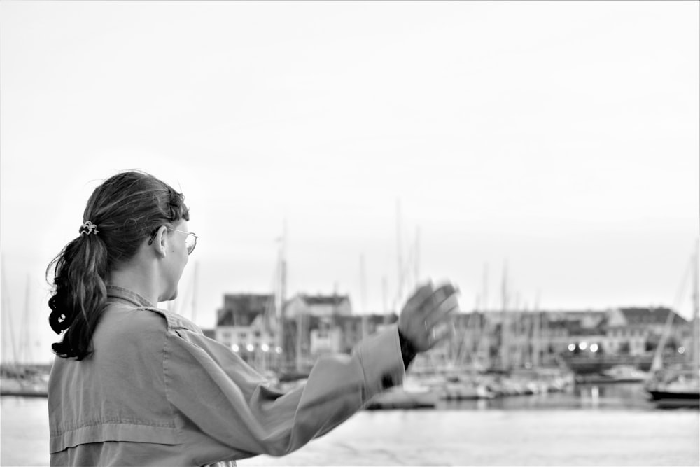 woman raising her right hand near body of water and buildings