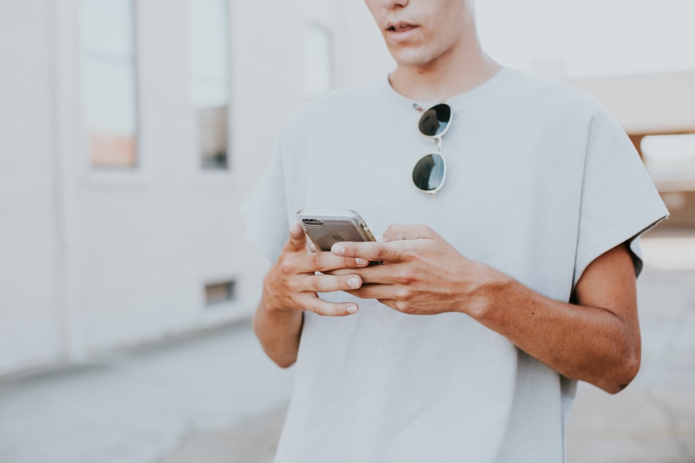 Hombre en top blanco de cuello redondo usando teléfono inteligente al aire libre
