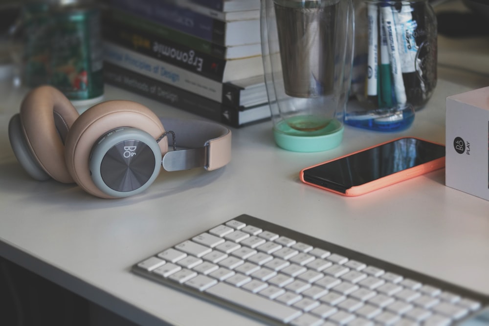 teclado de computador cinza e branco ao lado de fones de ouvido cinza