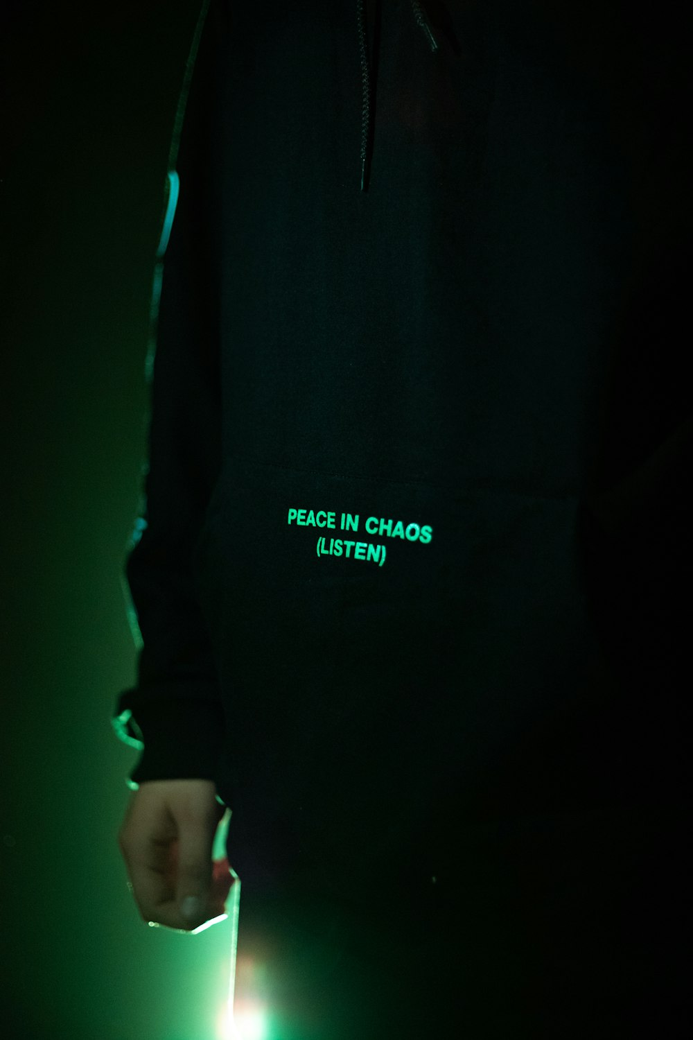 a person wearing a black hoodie with a green glow on it