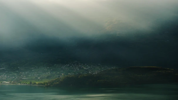 Golden sunlight filters through mist over Erhai Lake, with distant mountains framing a tranquil village pier.