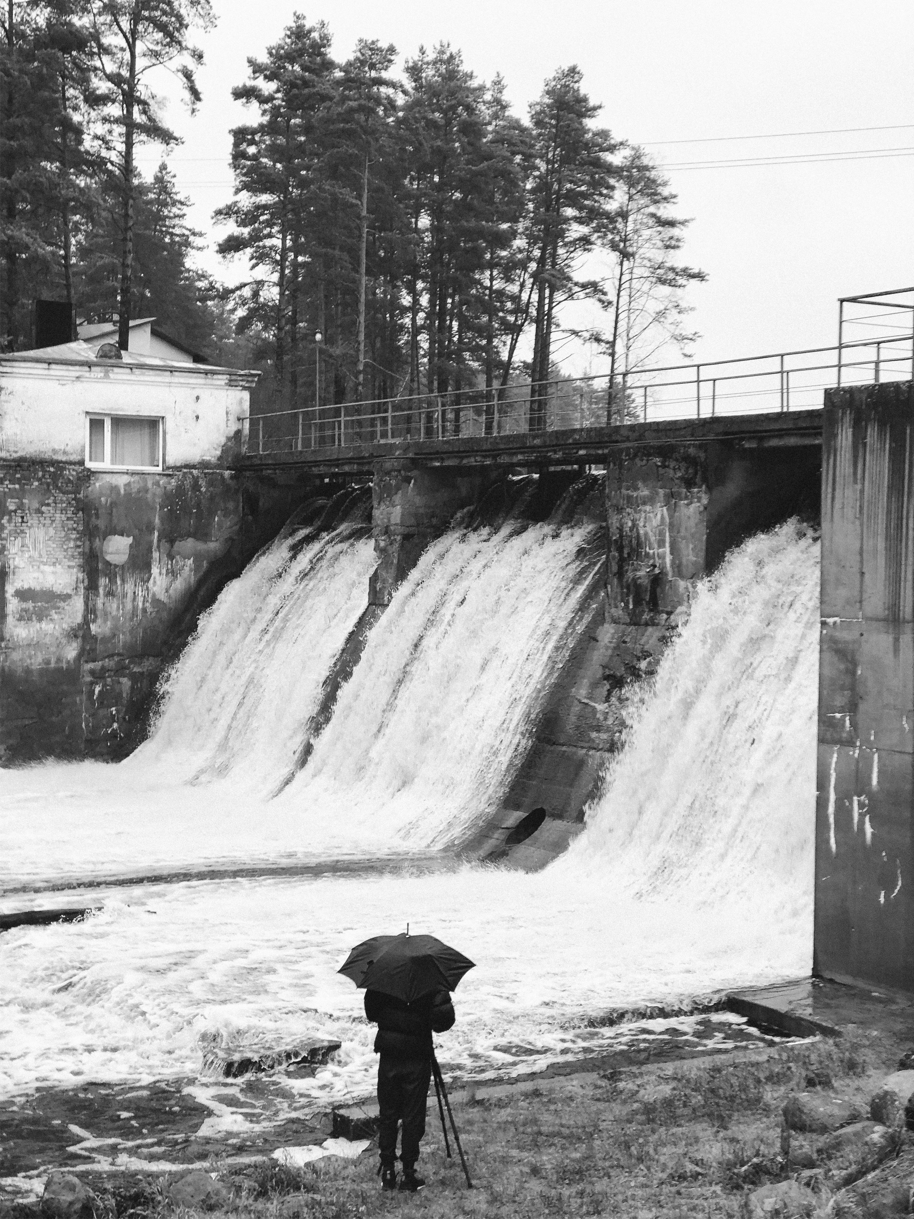 grayscale photo of person under umbrella in front of dam