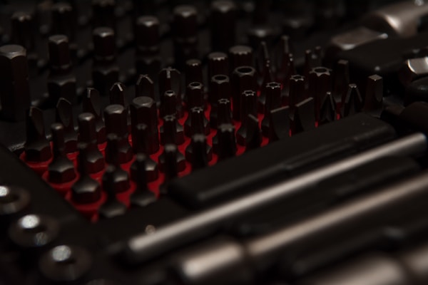 An assortment of shiny drill bits and hand tools laid out on a dark gray surface.