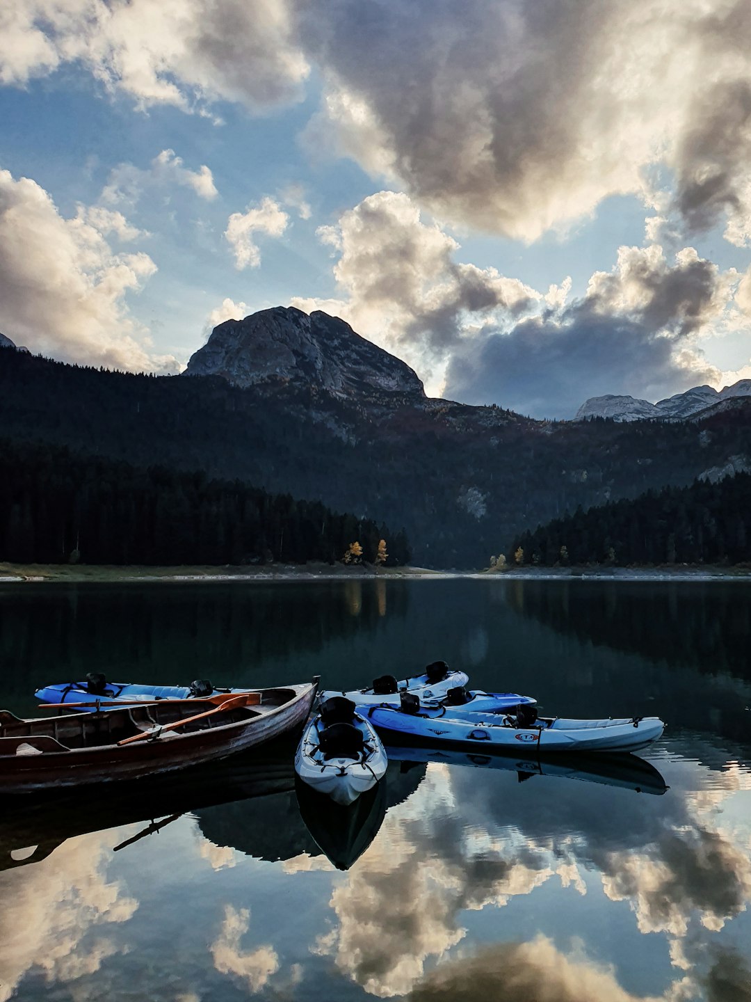 white and blue boat on lake near green trees and mountain under white clouds and blue