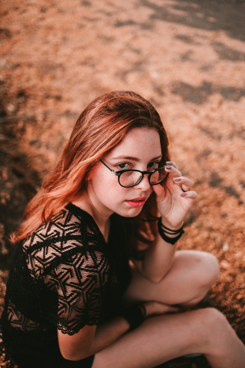 selective focus photography of sitting woman wearing black dress holding her eyeglasses