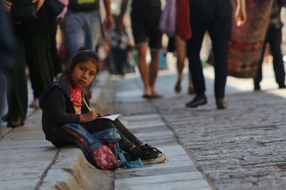 Selektive Fokusfotografie eines Mädchens, das tagsüber auf dem Gehweg sitzt