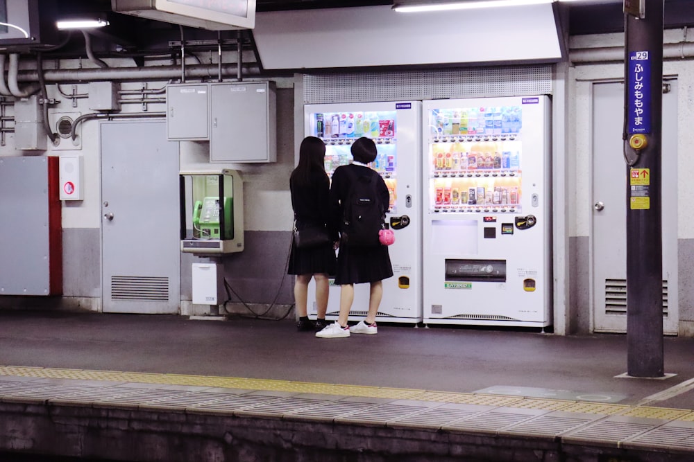 Due donne in abiti neri in piedi davanti al distributore automatico bianco