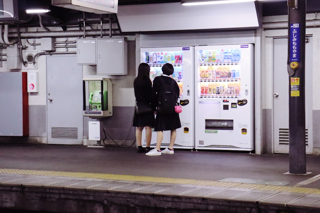 two women in black dresses standing in front of white vending machine