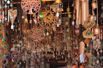 A variety of hanging ornaments and wind chimes are densely displayed, featuring intricate designs like trees, hearts, and flowers. These items are crafted from materials such as wood, metal, and glass, and are all suspended with price tags visible.