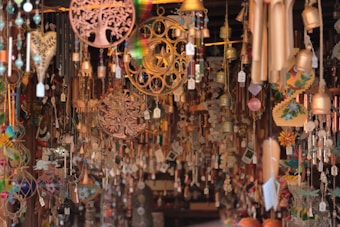 A variety of hanging ornaments and wind chimes are densely displayed, featuring intricate designs like trees, hearts, and flowers. These items are crafted from materials such as wood, metal, and glass, and are all suspended with price tags visible.