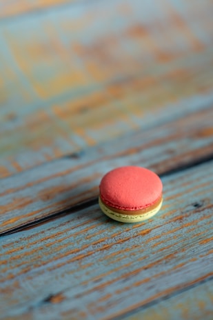 Close-up of a perfectly crafted macaron with delicate pastel colors on a rustic wooden table.