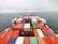 A large number of colorful shipping containers are neatly stacked on a cargo ship that is sailing on an open, calm ocean. The horizon is slightly foggy, giving a sense of distance and vastness.