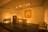 A minimalistic interior scene features traditional Asian furniture within a softly lit room. The setup includes a wooden table, chairs, and a small cabinet against a neutral-colored wall. A framed artwork with bamboo motifs hangs on the wall, enhancing the room's cultural aesthetic. Subtle lighting adds warmth and highlights the simplicity and elegance of the furnishings.