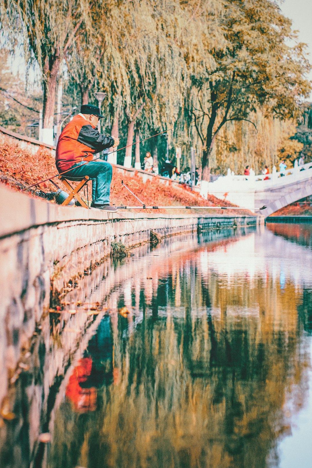 man wearing orange and black jacket fising on lake