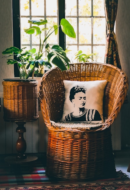 A serene bedroom corner with layered neutral-toned linens, a rattan chair, and a small indoor plant by the window.