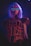 A person with a short white wig is wearing a futuristic outfit featuring neon pink and blue elements. The person is adorned with light-up glasses that have horizontal blue lines across the lenses, creating a cyberpunk aesthetic.