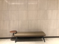 A padded shoe changing bench featuring a tufted cushion and sturdy wooden legs, set against a neutral wall.