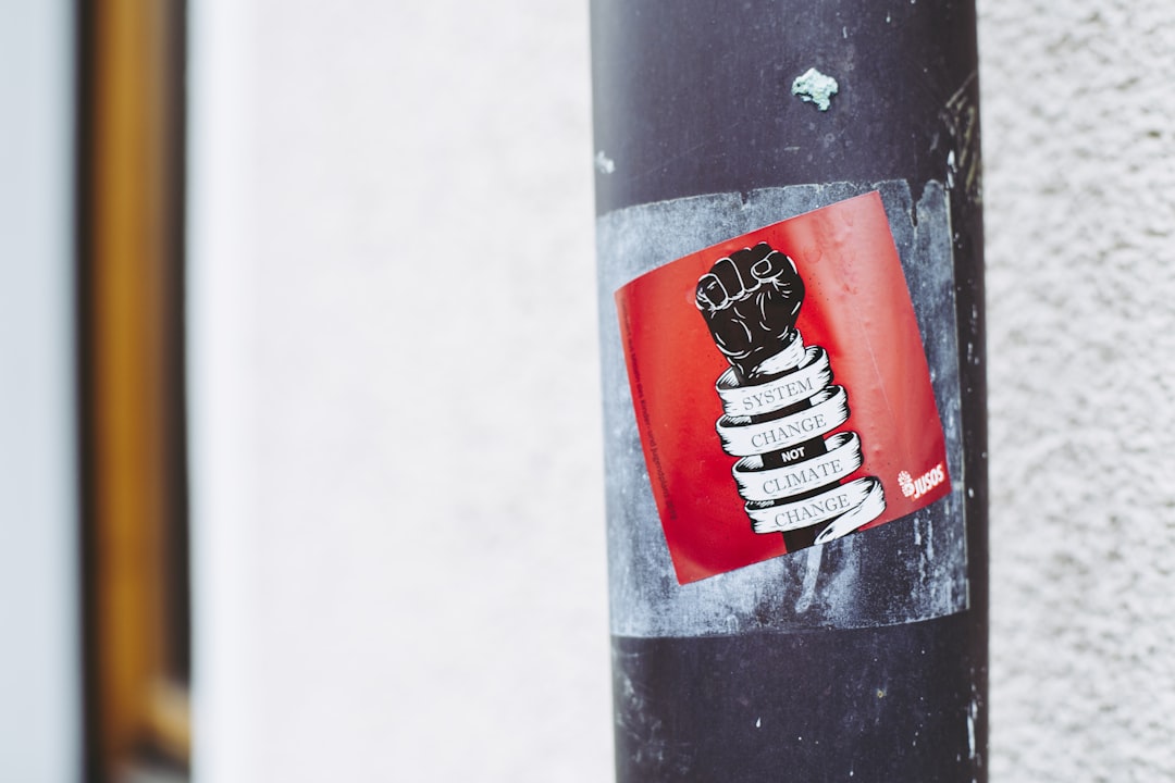 black and white fist-printed poster on a metal post, SYSTEM CHANGE NOT CLIMATE CHANGE. Civil disobedience – rebellion ag