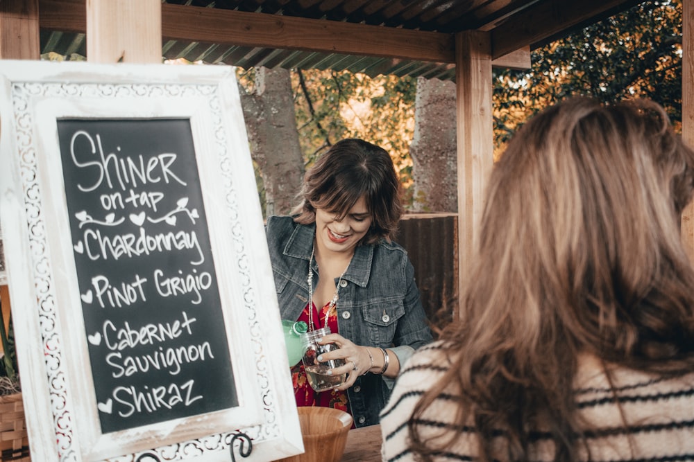 smiling woman pouring drink on cup beside sign