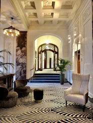 A hotel lobby with patterned carpet, armchairs, and an arched doorway leading to stairs
