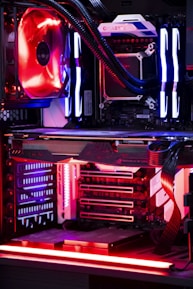 An internal view of a computer showing components like a graphics card, cooling system, and LED lighting. The setup features vibrant red and blue LED lights and a structured, high-tech arrangement with clearly visible branding on the components.