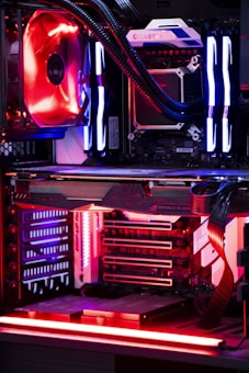 An internal view of a computer showing components like a graphics card, cooling system, and LED lighting. The setup features vibrant red and blue LED lights and a structured, high-tech arrangement with clearly visible branding on the components.
