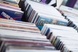 Rows of vinyl records are tightly packed in a display rack, each encased in protective sleeves. The covers feature various colorful and artistic designs indicating diverse music genres.