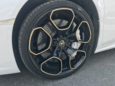Close-up of a luxury car’s polished wheel and brake caliper, reflecting the gold and silver accents of the brand.
