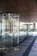 A series of glass revolving doors reflecting the outside street scene, with a modern design and metal frames. The clean architectural lines of the building and its ceiling panels are visible with reflections of the street creating a dynamic interplay of glass and light.