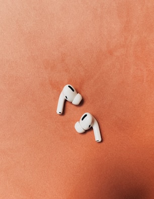 Modern wireless earbuds resting on a bold orange background.