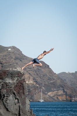 Cliff jumpers mid-air above sparkling blue sea, with a boat waiting nearby.