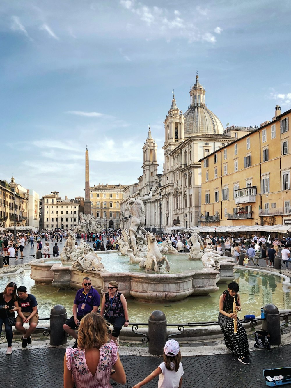 people walking and sitting near water fountain during daytime