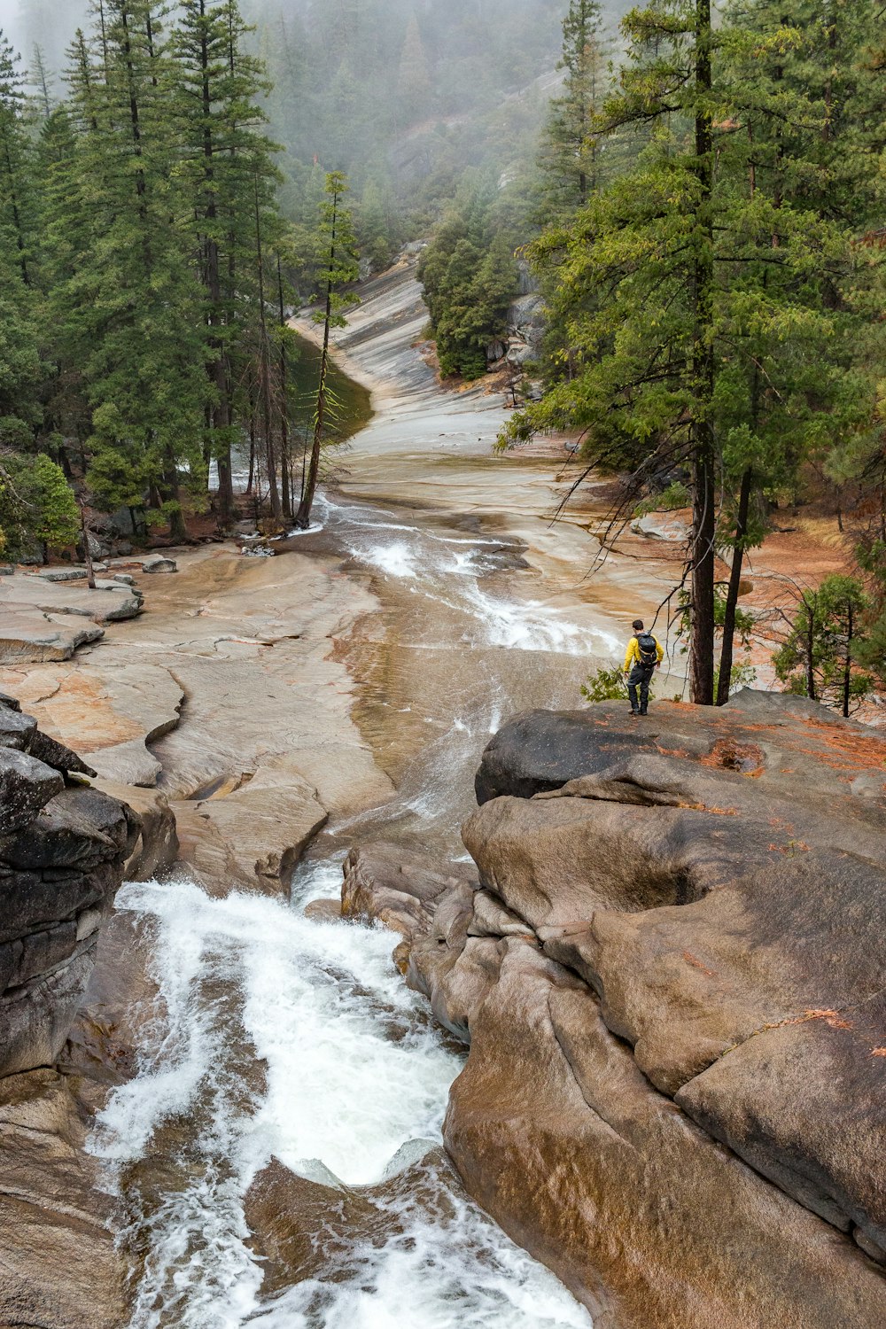 person in yellow jacket standing on rock near river during daytime