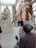An artist is sketching a sculpture inside a sunlit gallery with high ceilings and large windows. The sculpture depicts a group of intertwined figures, and the artist appears focused on capturing its details. Other visitors are observing various artworks in the lively museum environment.