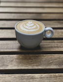 Close-up of a frothy cappuccino with latte art on a rustic wooden table.