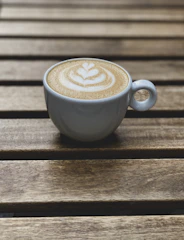 Close-up of a steaming cappuccino with latte art on a rustic wooden table.