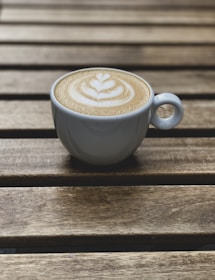 A steaming cup of cappuccino with intricate latte art on a rustic wooden table.
